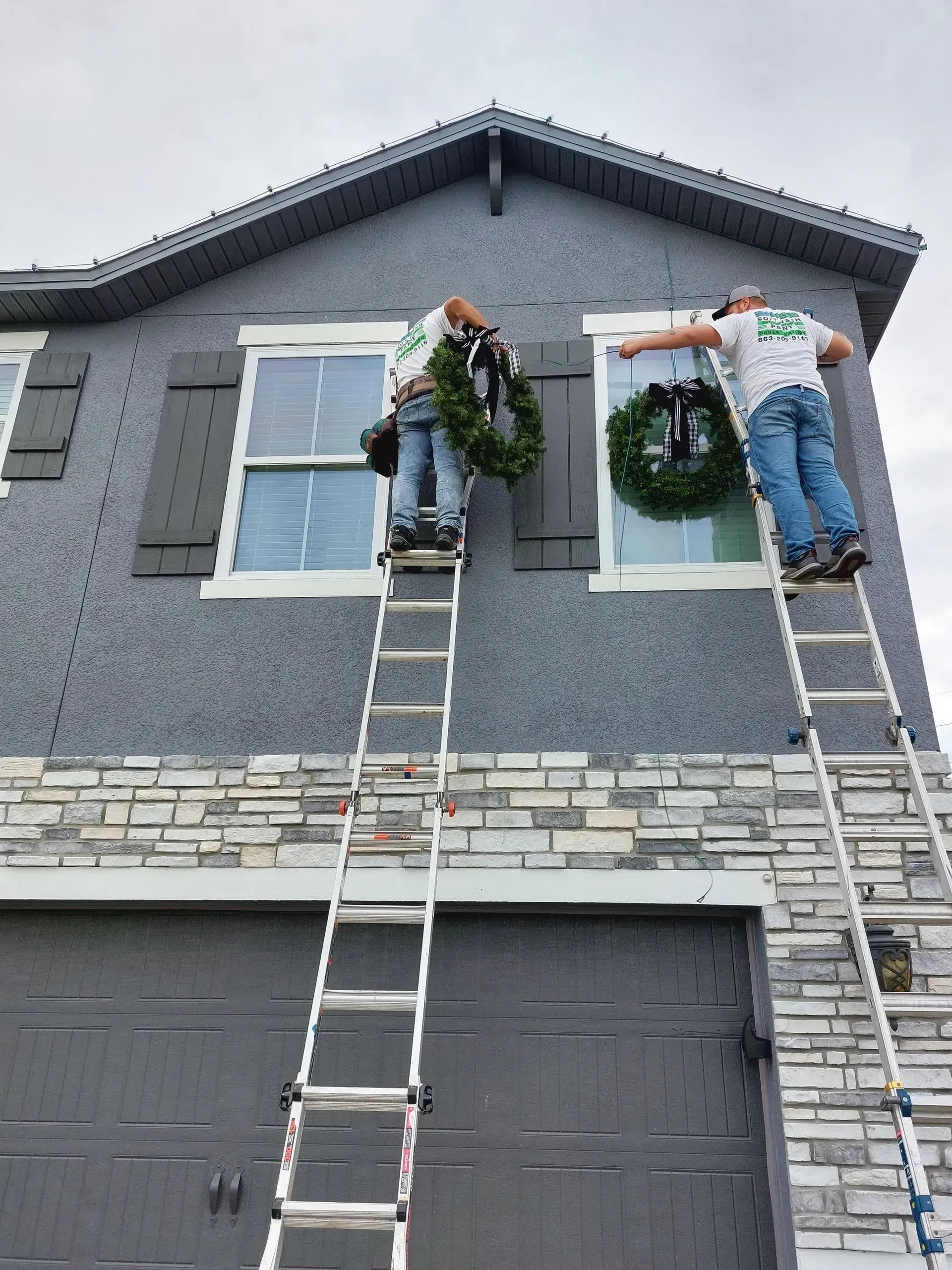 Two men on ladders decorating a house with a wreath