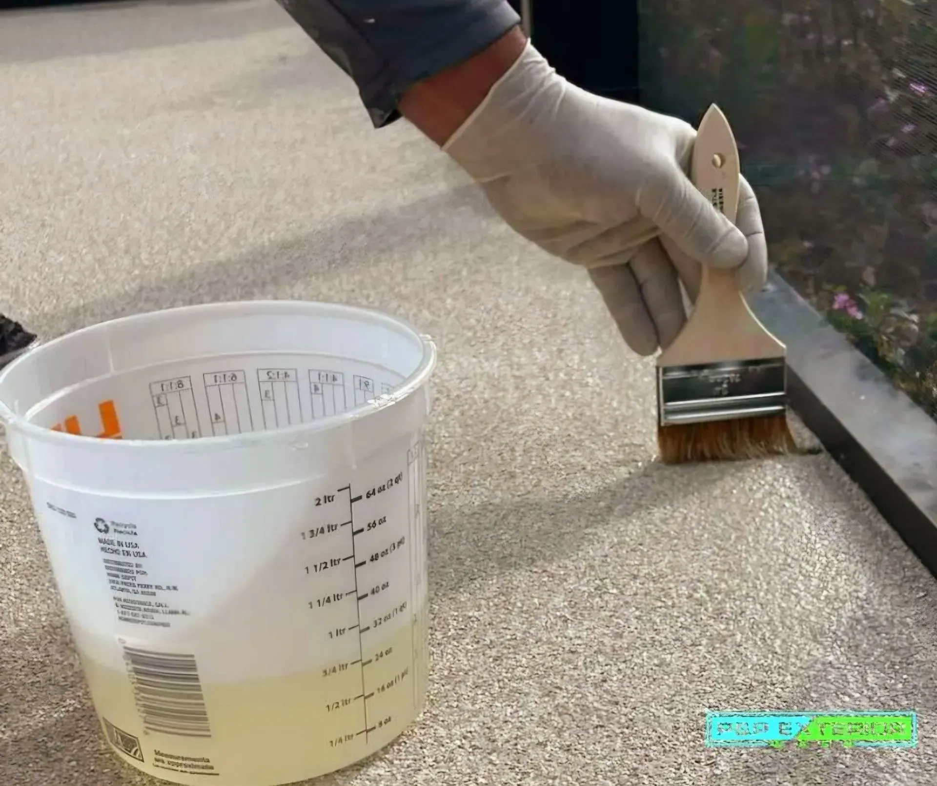 A person is holding a brush next to a measuring cup filled with liquid.