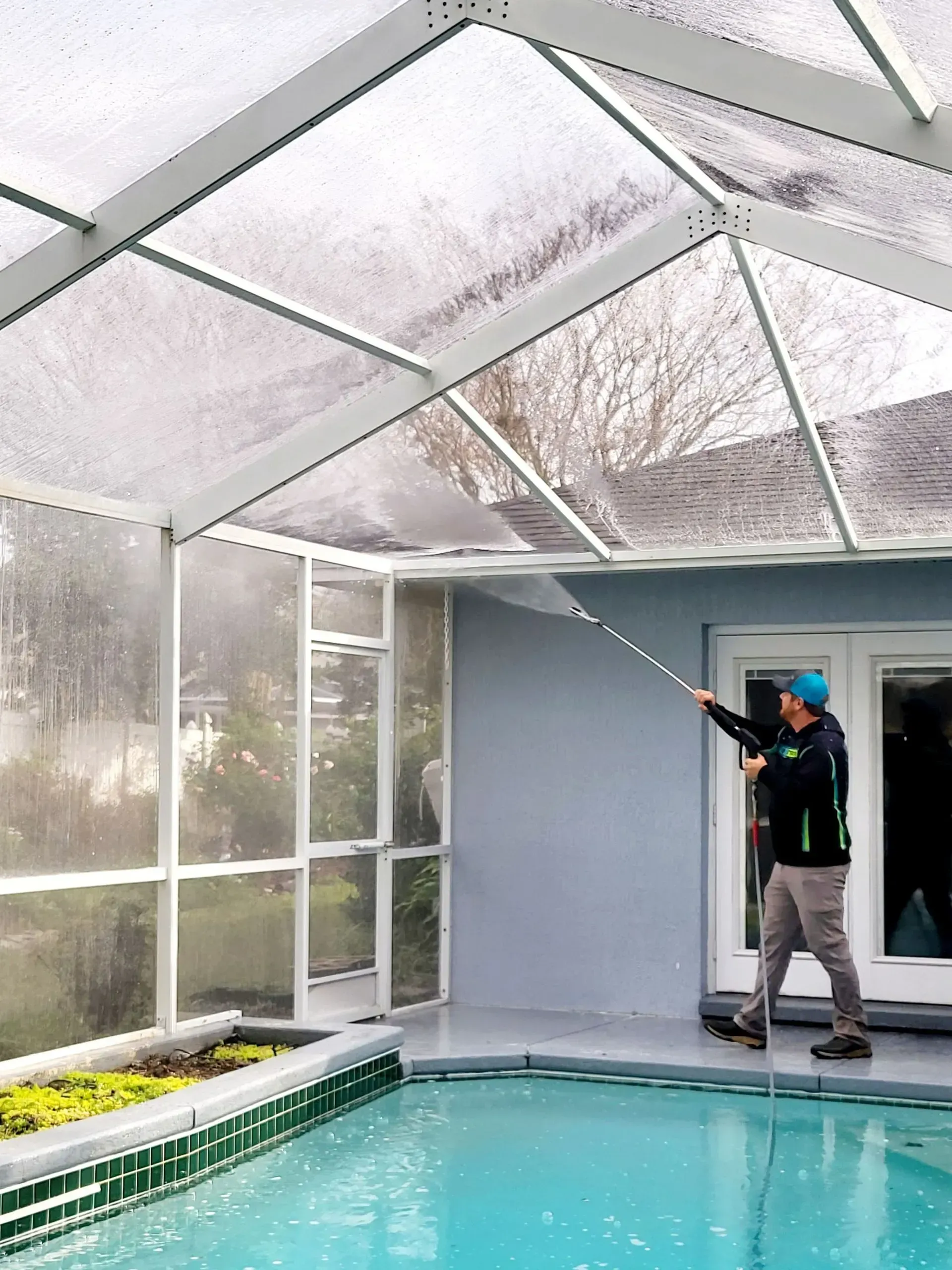 A man is cleaning a screened in swimming pool with a hose.