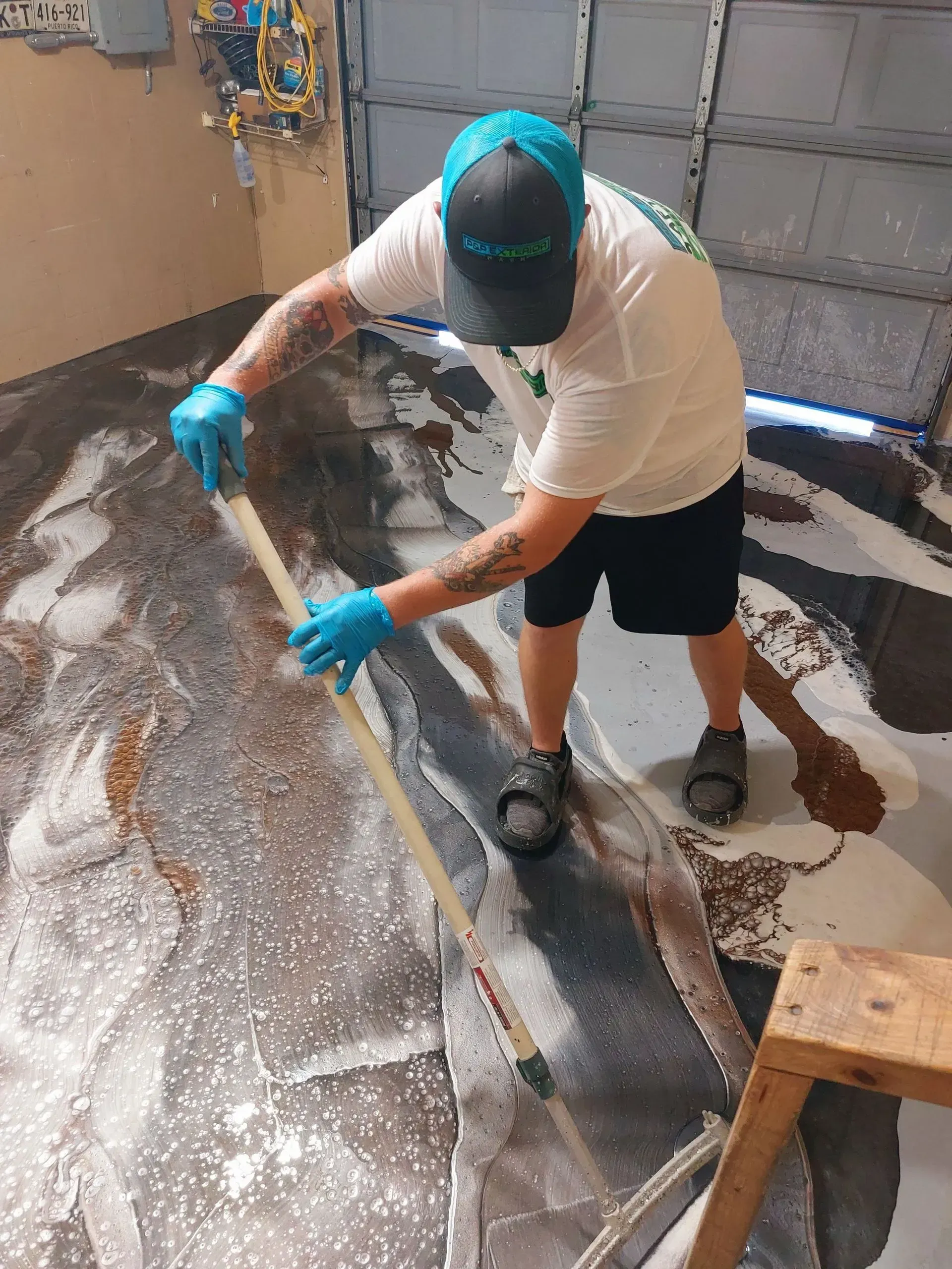 A man is painting a garage floor with a broom.