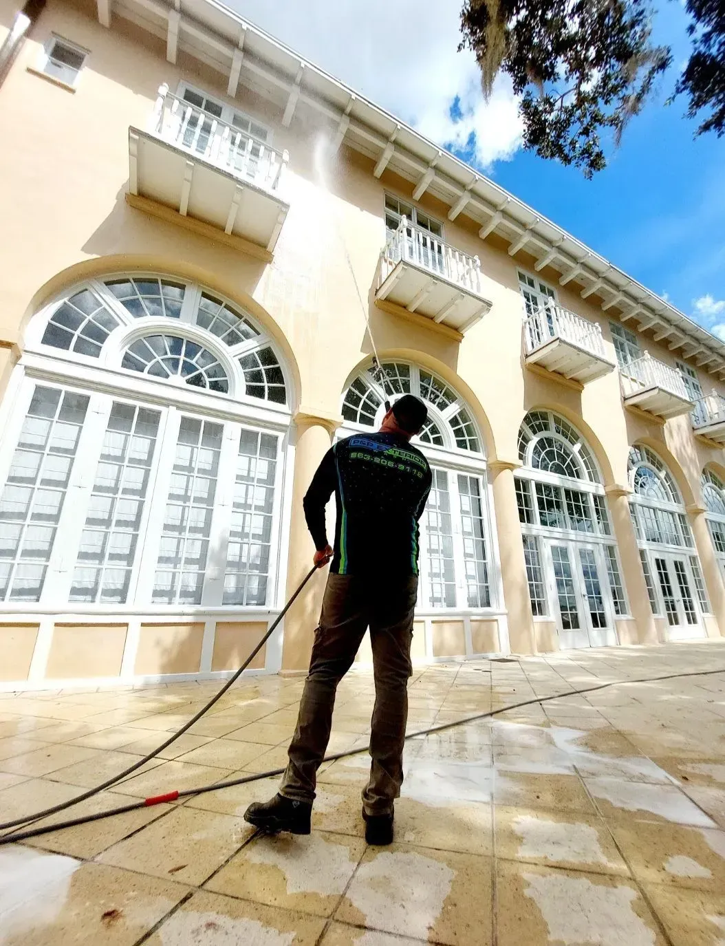 A man is cleaning the sidewalk in front of a large building.