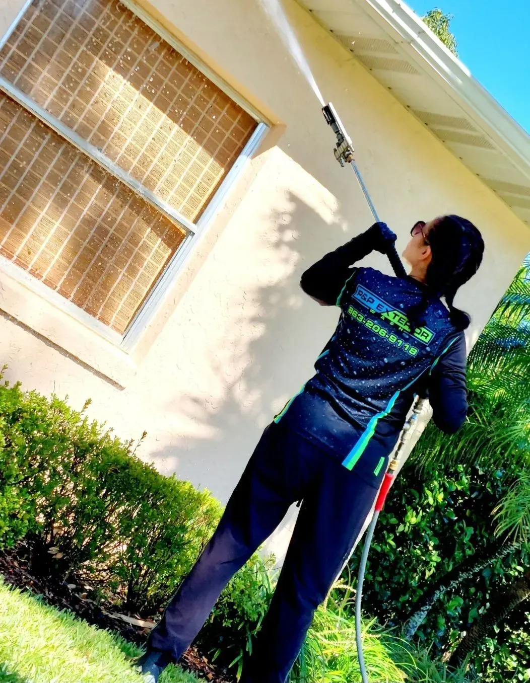 A woman is cleaning the side of a house with a pressure washer.