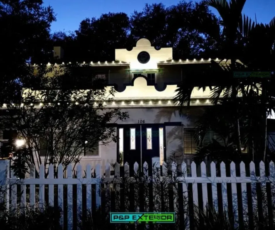 A white picket fence surrounds a house that is lit up at night