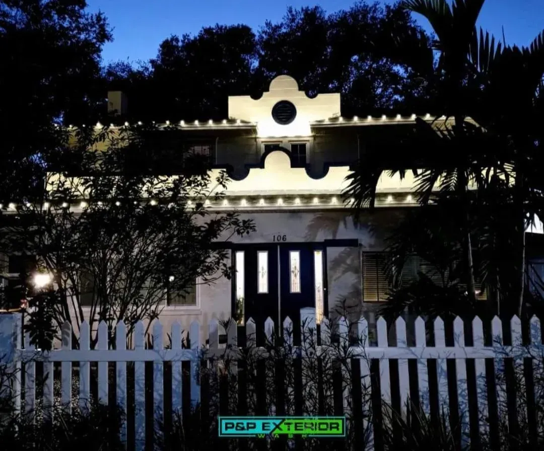 A white picket fence surrounds a house that is lit up at night
