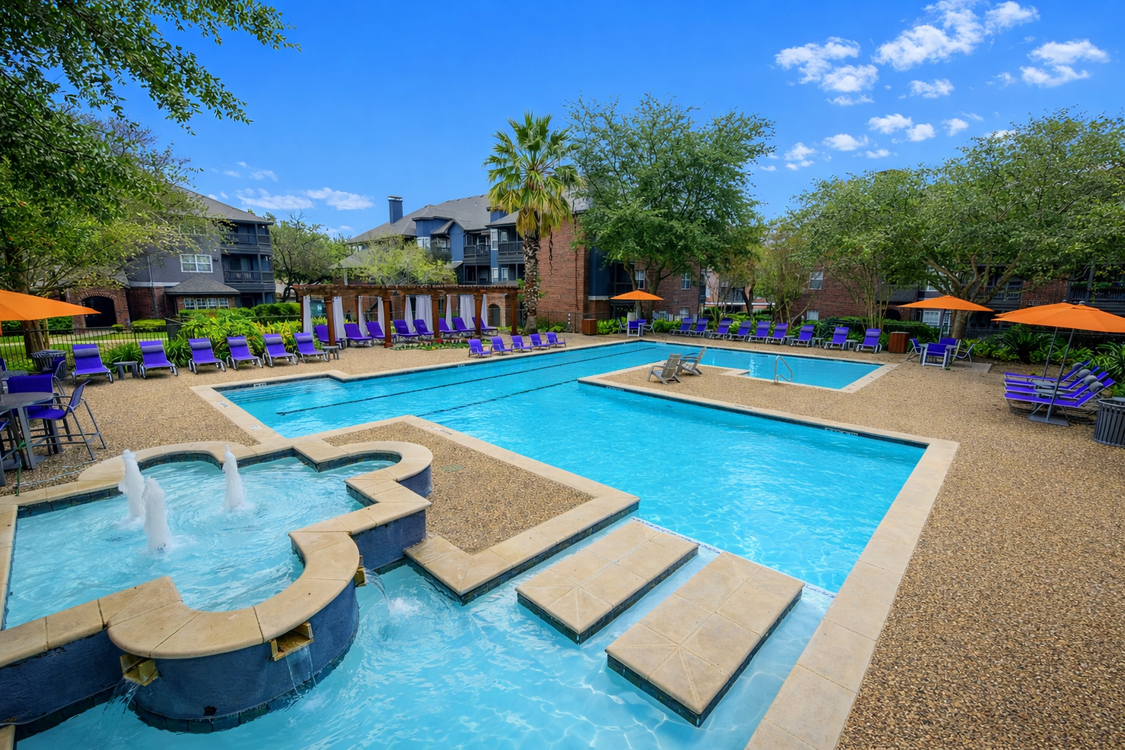 A large swimming pool with stairs and umbrellas in front of a building at Alon at Castle Hills.