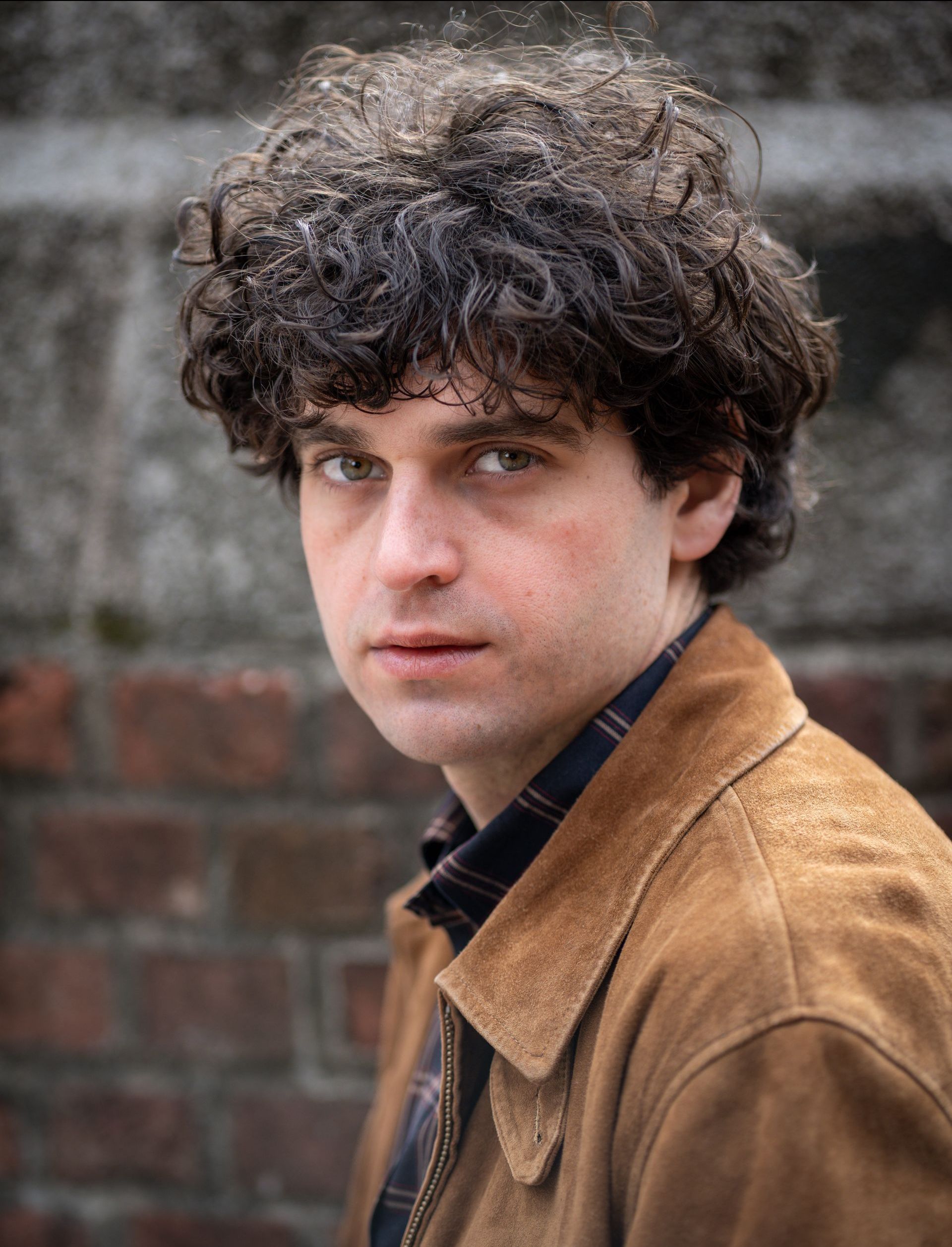 Riley Scott looking at the camera in a suede jacket 