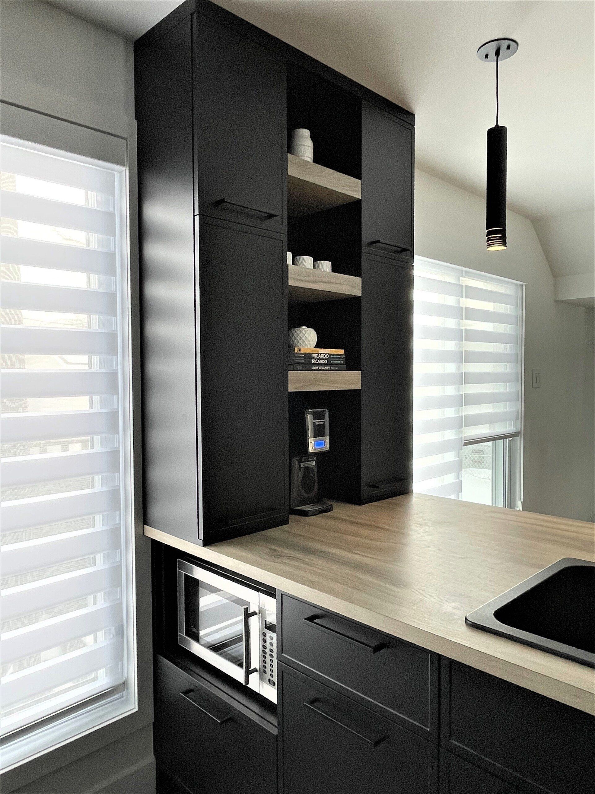Cuisine moderne avec armoires sombres, étagères ouvertes et micro-ondes intégré.