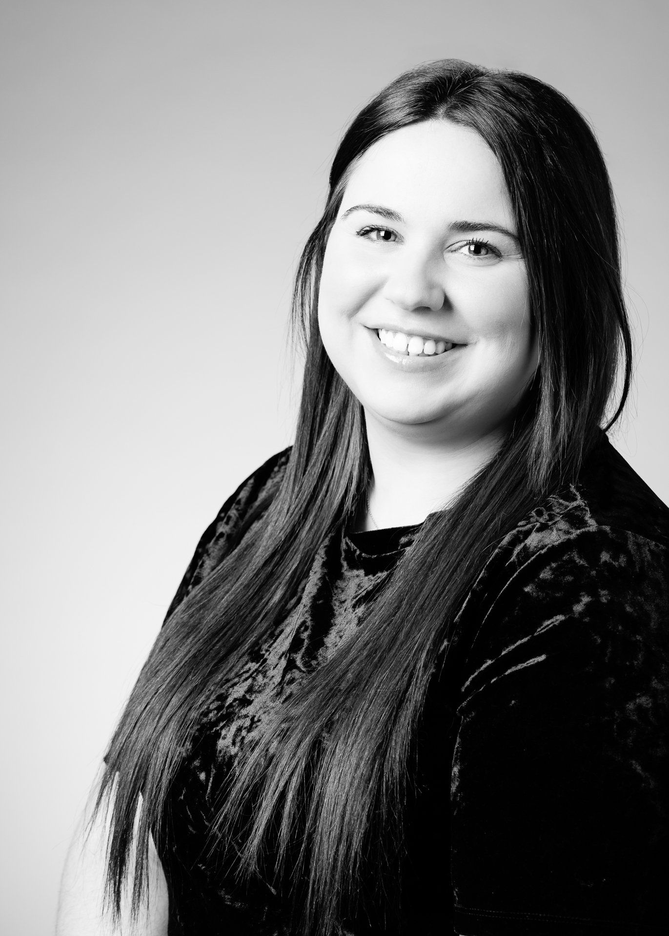 Une femme aux longs cheveux noirs sourit à la caméra ; elle porte un haut foncé et texturé.