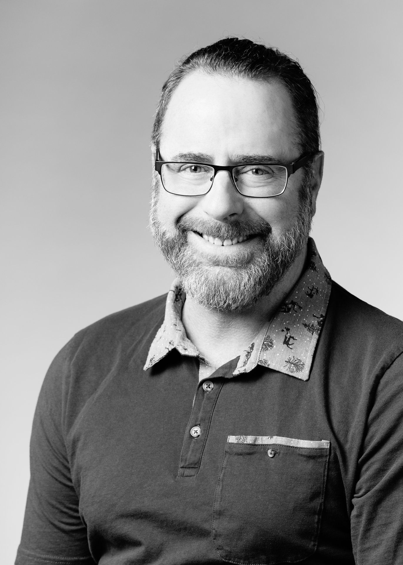 Homme avec des lunettes et une barbe souriant, portant un polo.