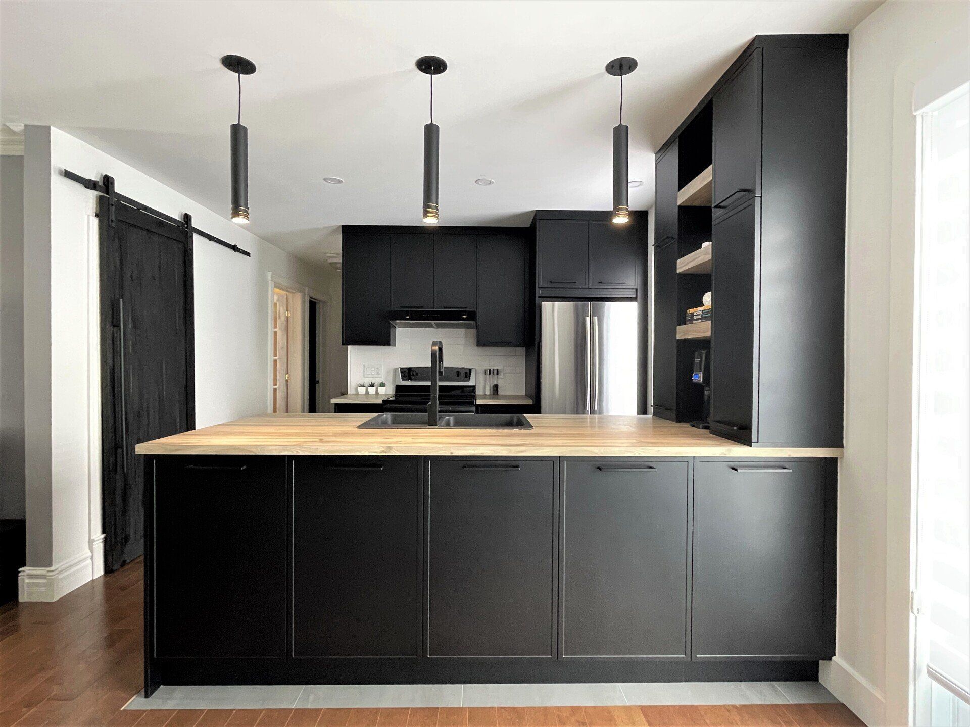 Cuisine moderne avec armoires noires, comptoir en bois et appareils électroménagers en acier inoxydable.