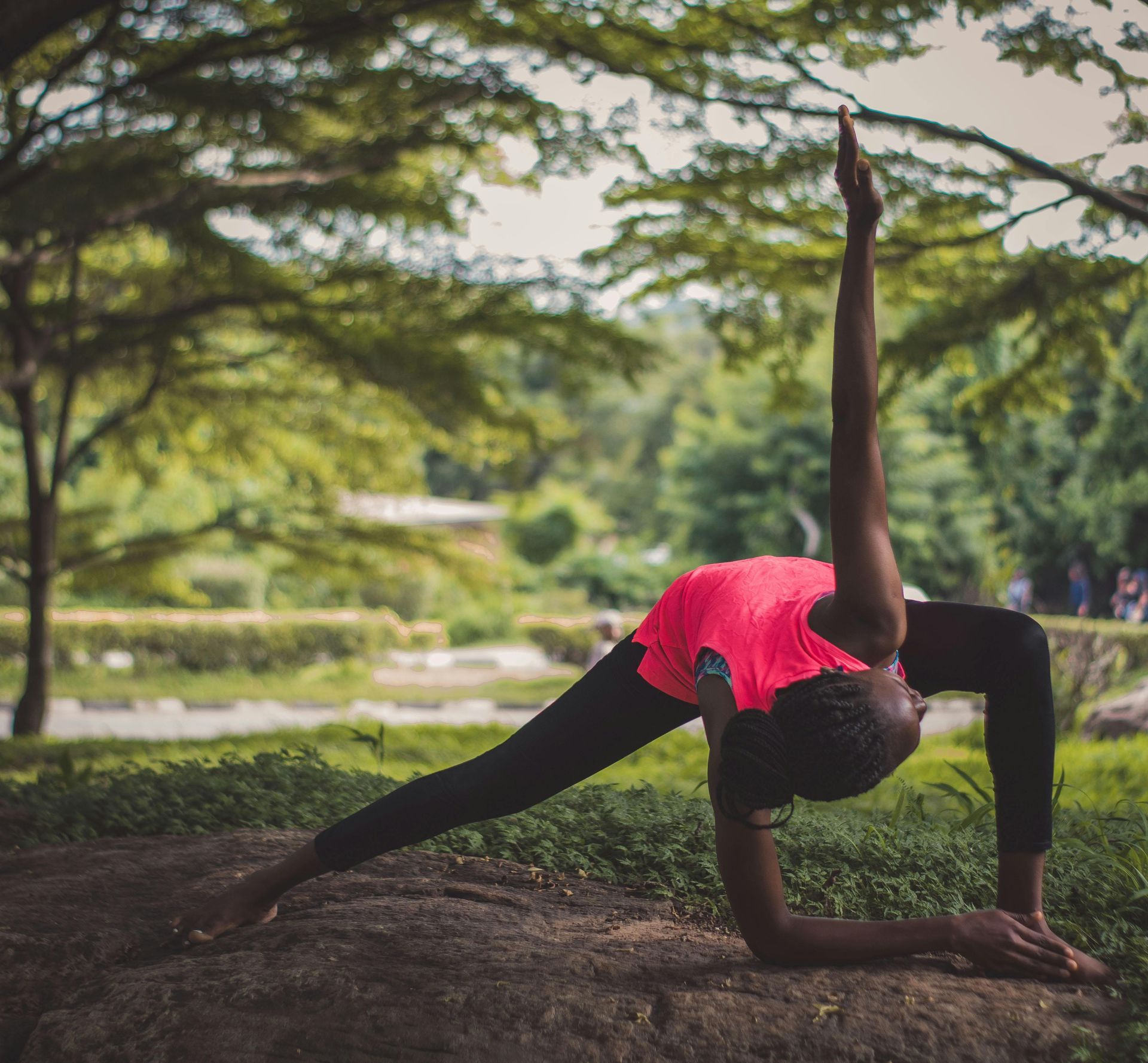 A woman in a pink shirt and black pants is doing yoga in a park.