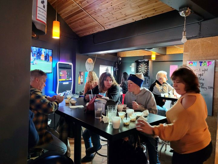 People seated around a table in a cozy bar, chatting with drinks under warm hanging lights.