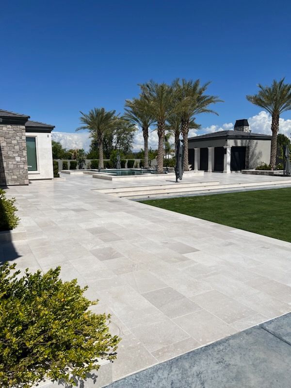 Stone patio with green grass, palm trees, and a building on a sunny day.