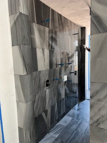 Gray and black tiled shower under construction; includes shower fixtures and a glimpse of the exterior.