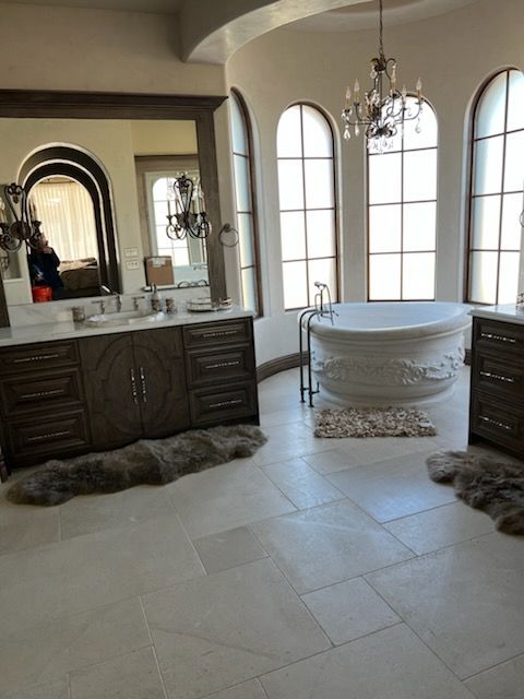 Luxurious bathroom with round tub, arched windows, chandelier, wood vanity, and sheepskin rugs.