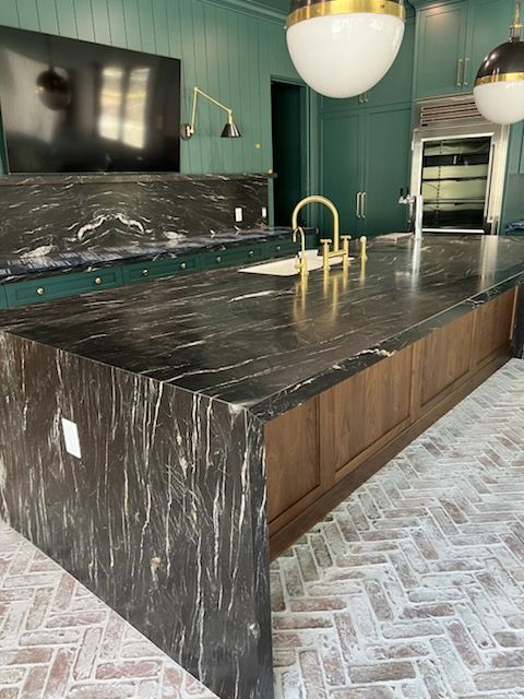Kitchen with black granite island, gold faucet, and brick herringbone floor.
