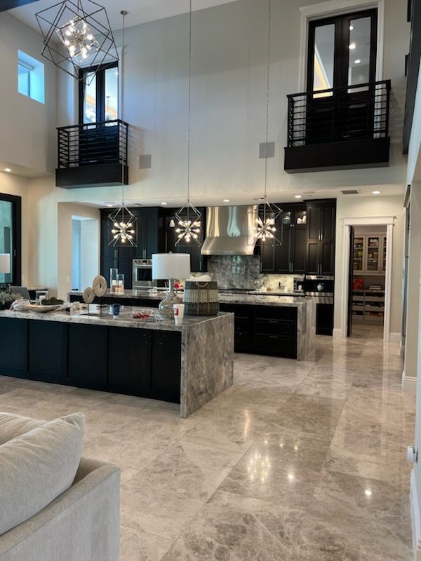 Spacious modern kitchen with dark cabinets, large island, and polished marble floors. Two balconies above.