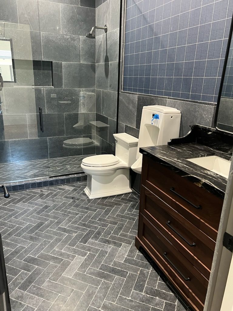 Bathroom with blue tile walls, herringbone floor, shower, toilet, and dark wood vanity.