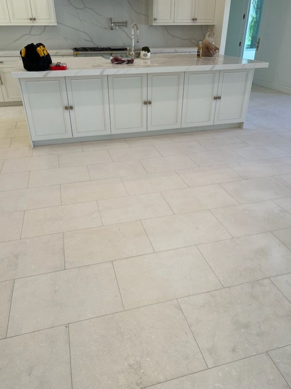White tiled kitchen floor, island with cabinets, light countertops, and tools.