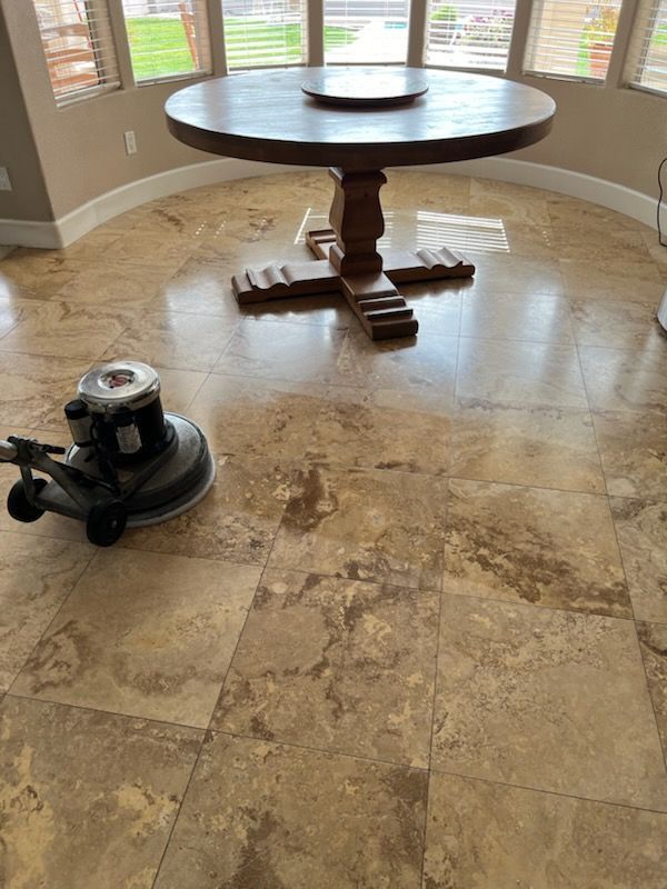 A floor polisher cleaning a shiny, patterned stone floor. A large wooden table sits in the background.