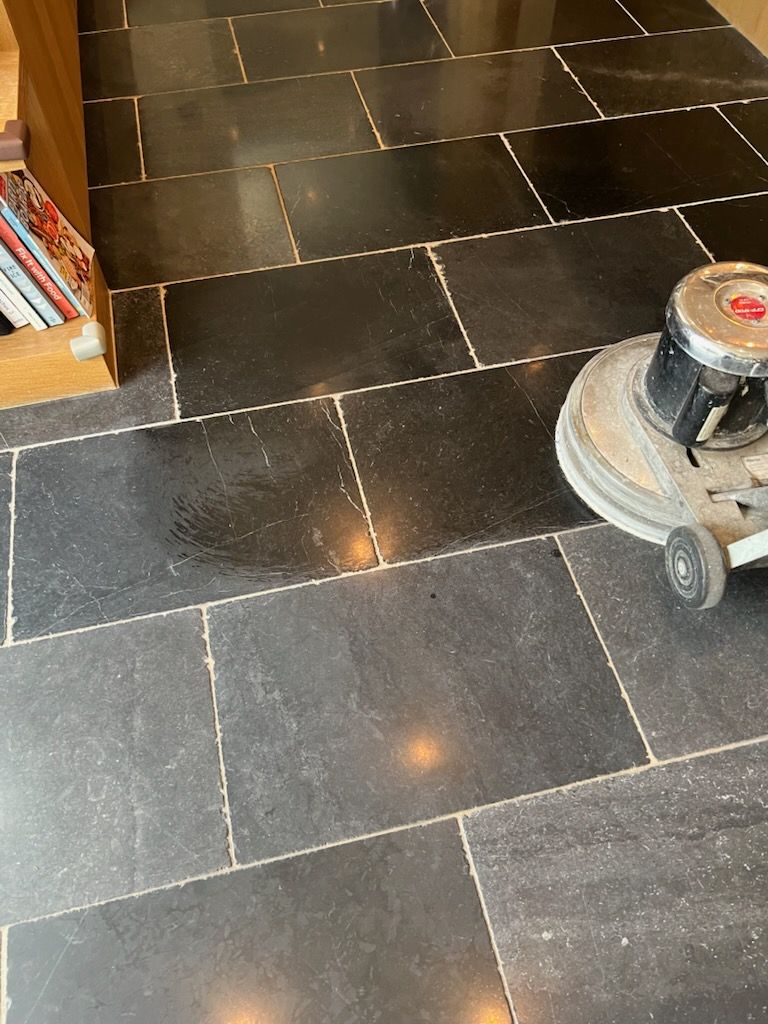 Black stone tile floor being cleaned with a floor buffer machine.