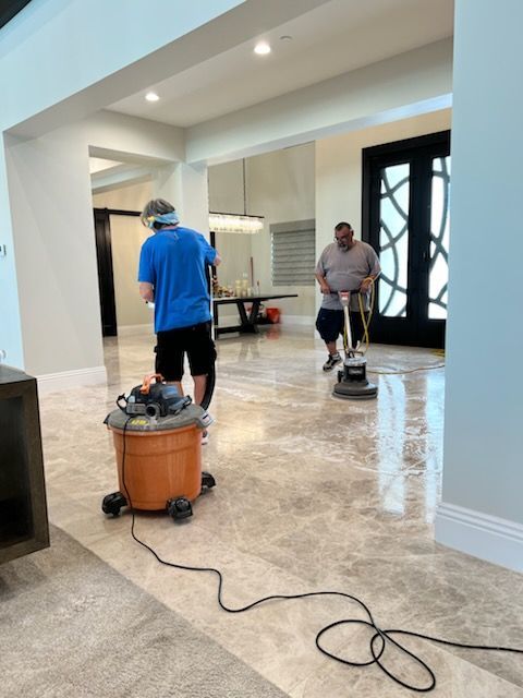 Two people cleaning a marble floor in a large room with a vacuum and floor buffer.
