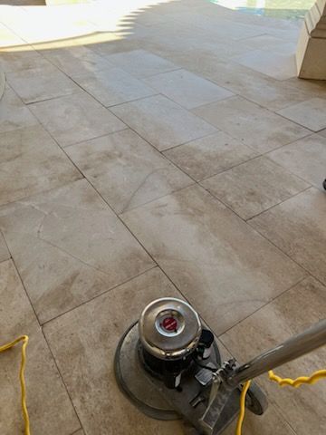 A floor cleaning machine scrubbing a light-colored tile patio.