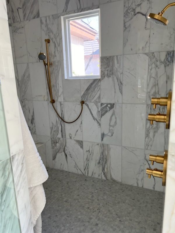 Marble tiled shower with brass fixtures, window, and a white towel.