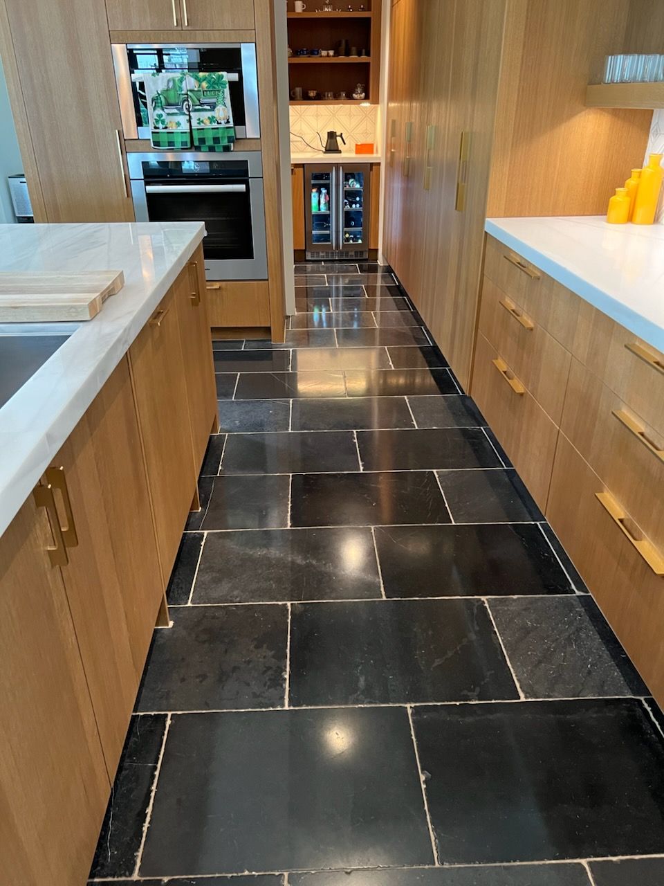 Kitchen with black tiled floor, light wood cabinets, and white countertops.