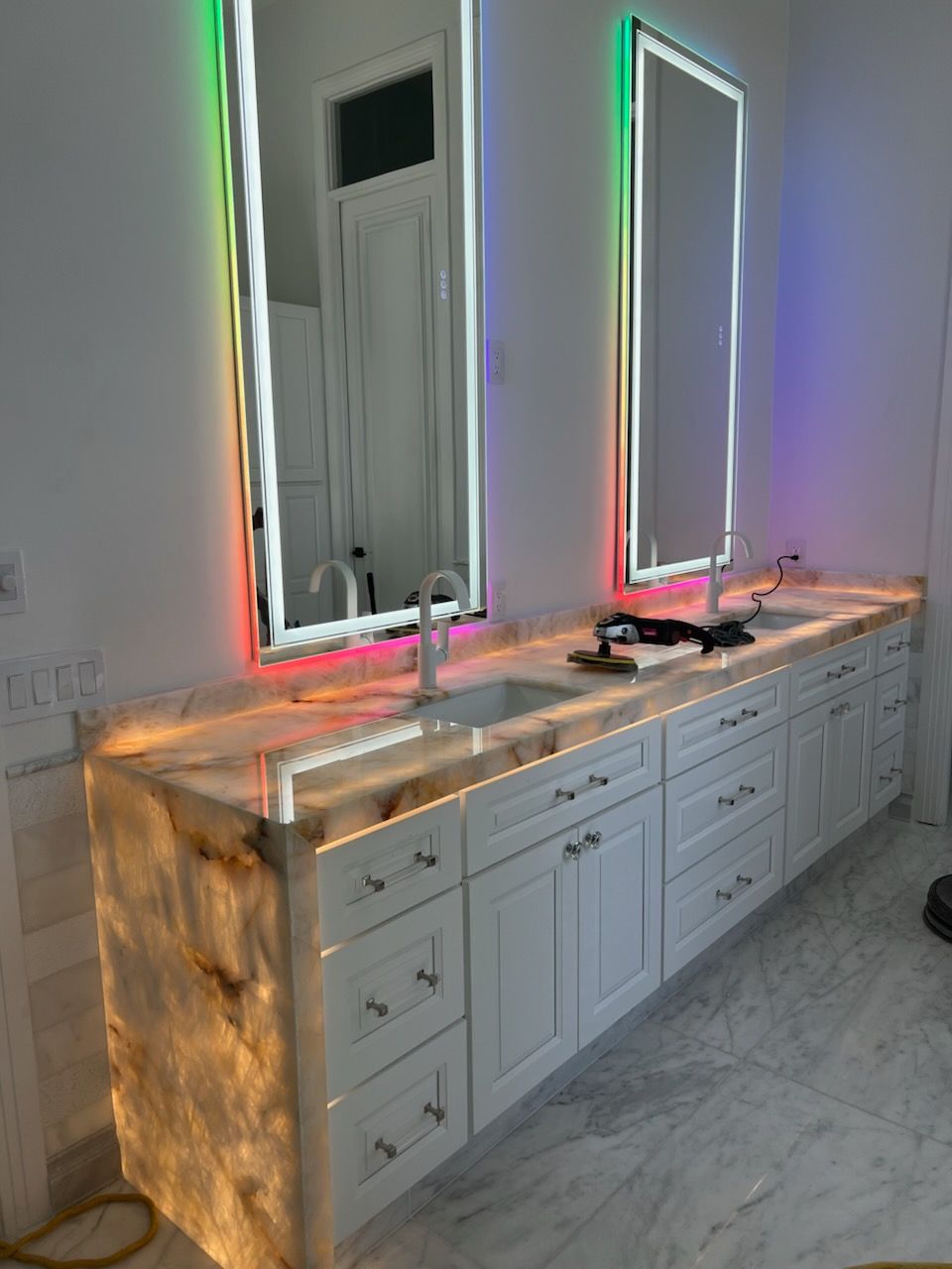 Double vanity bathroom with illuminated mirrors and countertop, white cabinets.