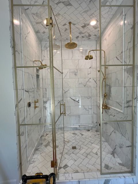 Luxurious shower with marble tiles, gold fixtures, and glass doors.