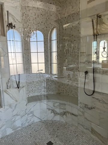 Luxurious bathroom with marble walls, arched windows, and a glass shower.
