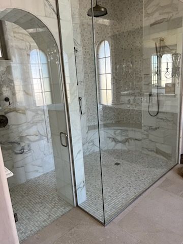 Luxurious shower with marble and mosaic tile, glass walls, and an arched window.