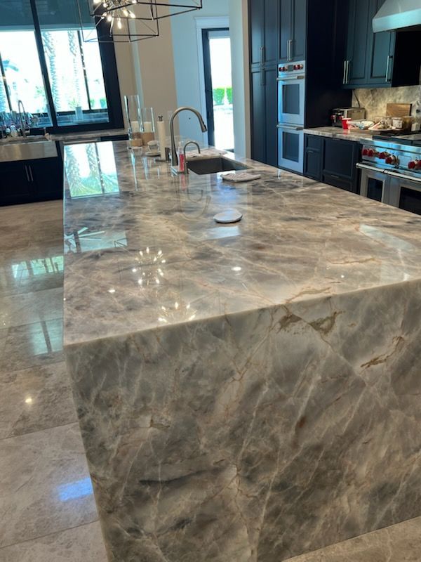 Gray marble kitchen island with sink, in a modern kitchen with dark cabinetry and stainless steel appliances.