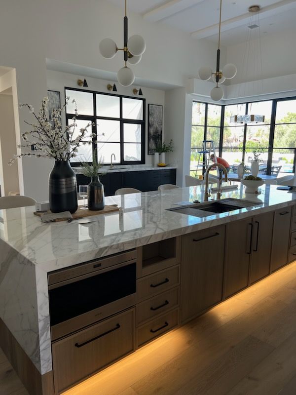 Modern kitchen with marble island, wooden cabinets, and black-framed windows.