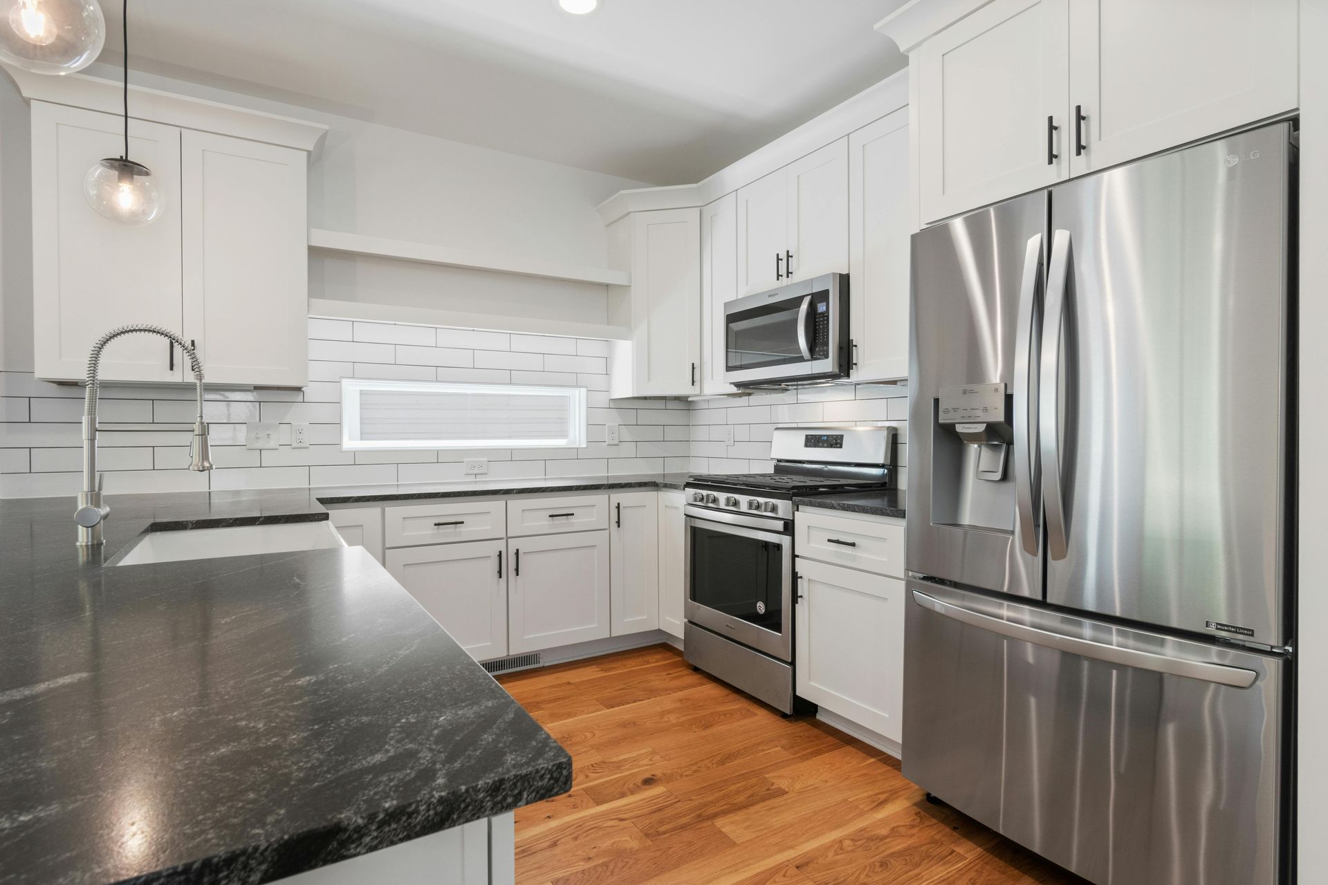 White kitchen with stainless steel appliances, dark countertops, and wood floors.