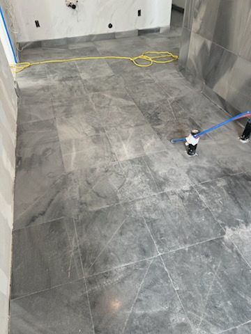 Gray tiled floor in a room under construction, with a yellow cord and support jacks visible.