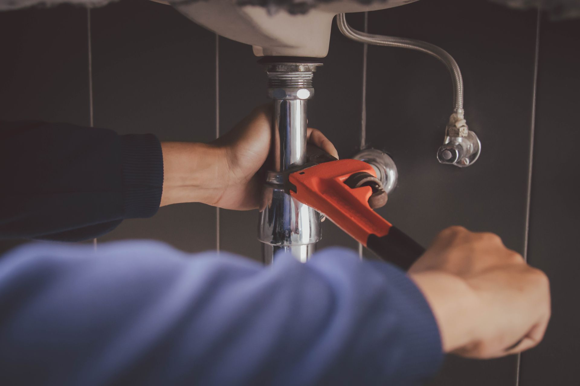 Hands using a wrench to tighten a pipe under a sink.