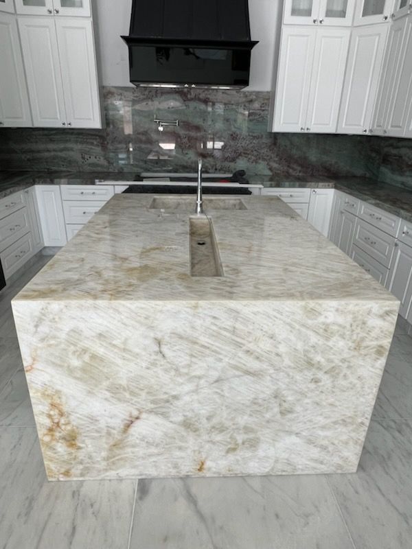 Kitchen island with a light-colored, patterned countertop. White cabinets and dark range hood in the background.