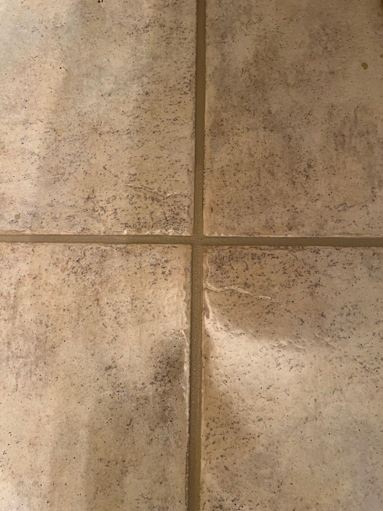 Tan ceramic tile floor with visible grout lines and dark spots.