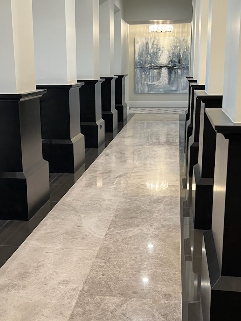 Long hallway with grey marble floor and black pillars. Abstract artwork hangs at the end.