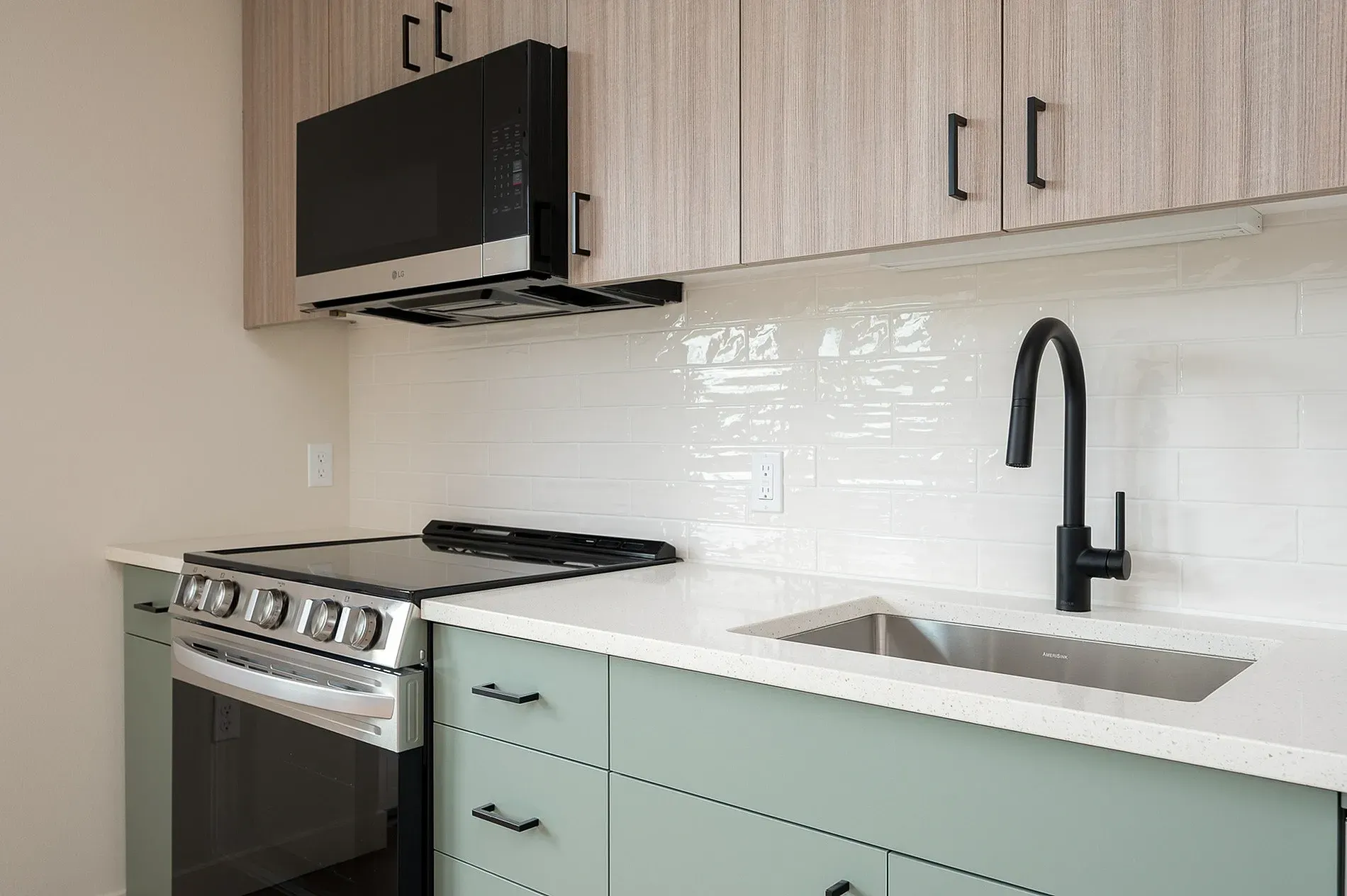 Modern kitchen with stainless steel stove, white subway tile backsplash, and sage green cabinets.
