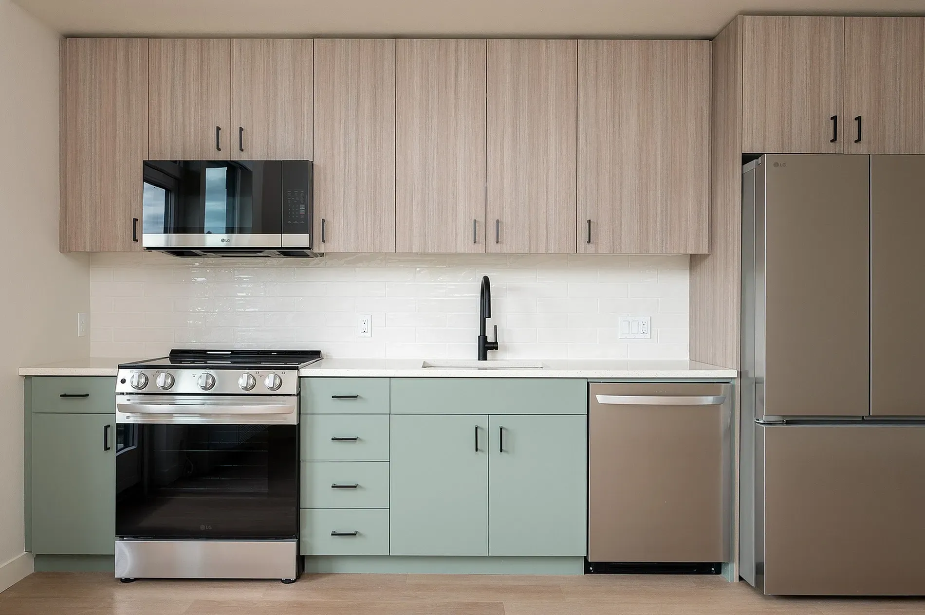 Modern kitchen with stainless steel appliances, light wood cabinetry, and sage green lower cabinets.
