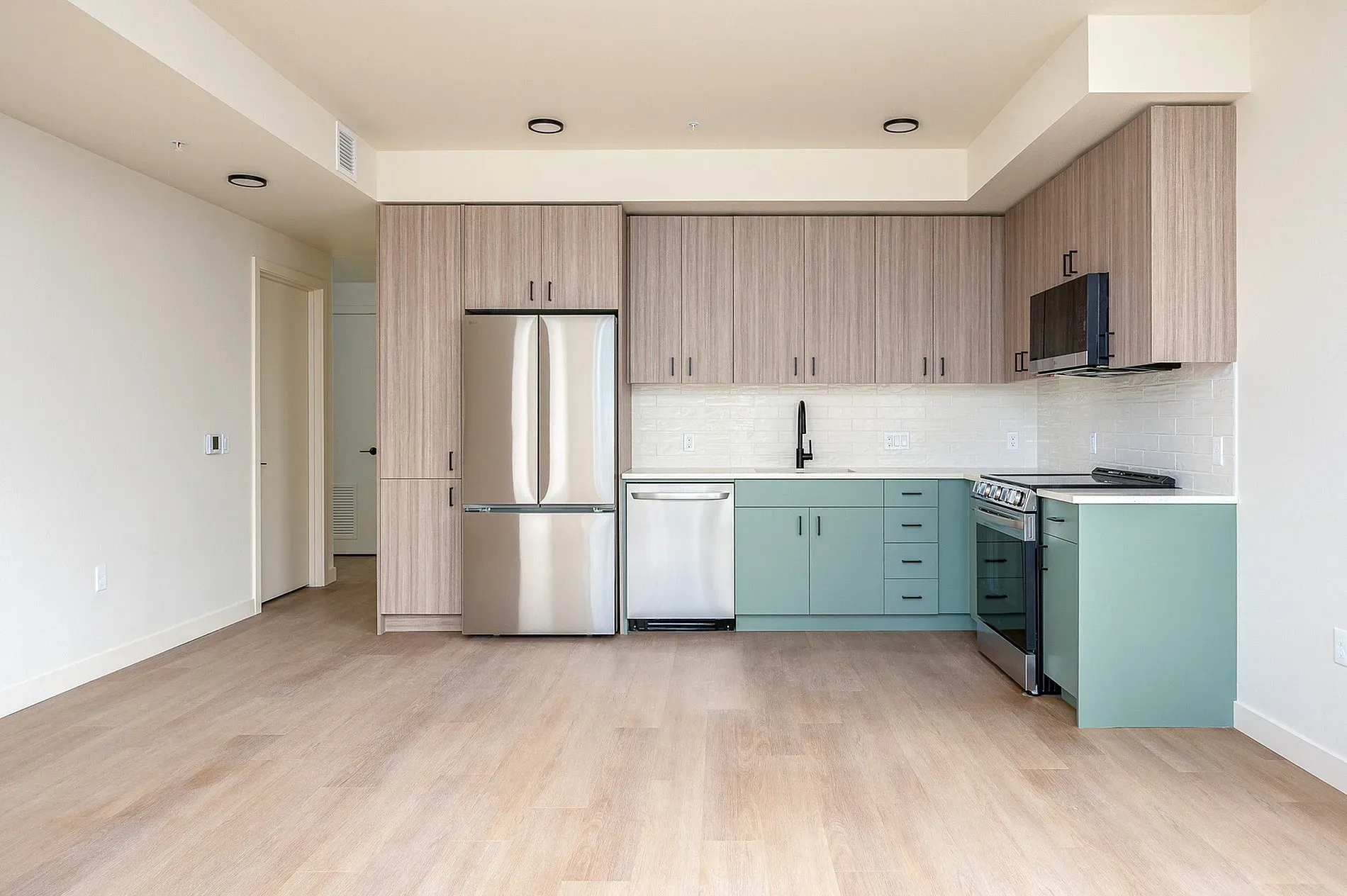 Modern kitchen with stainless steel appliances, light wood cabinets, and mint green lower cabinets.