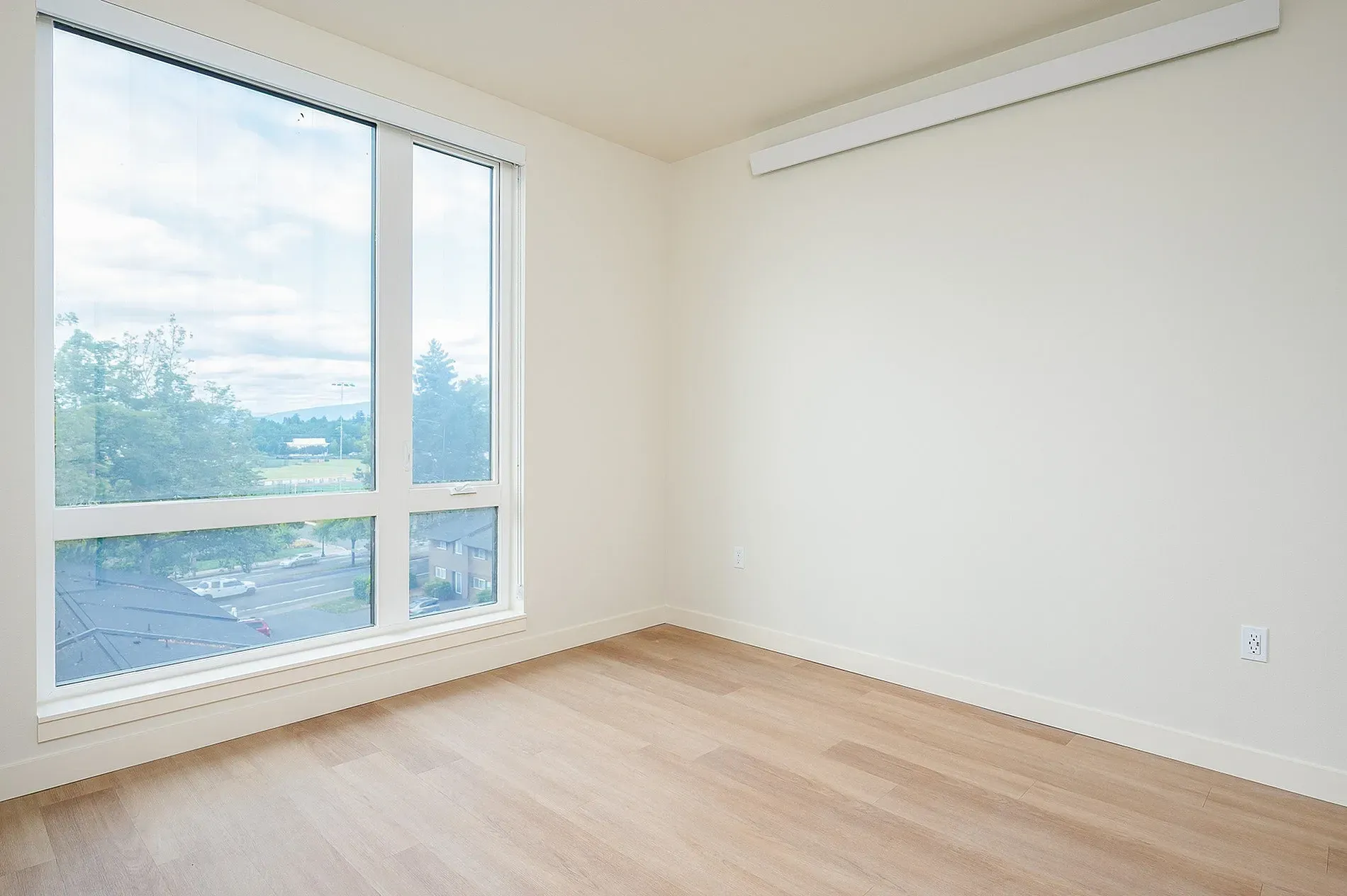 Empty living room with large window and light wood floors.