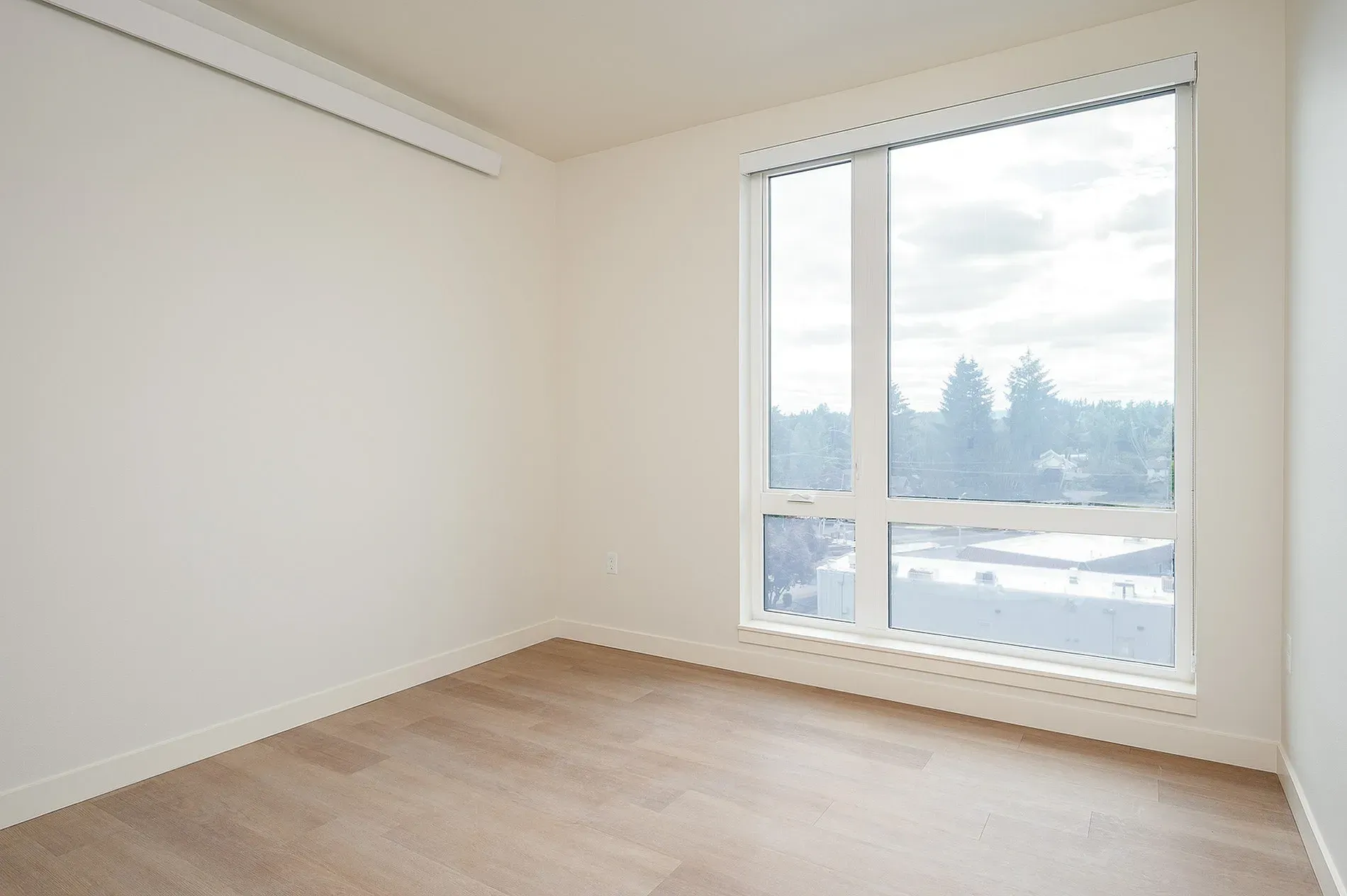 Empty room with a large window offering a view of trees and buildings.