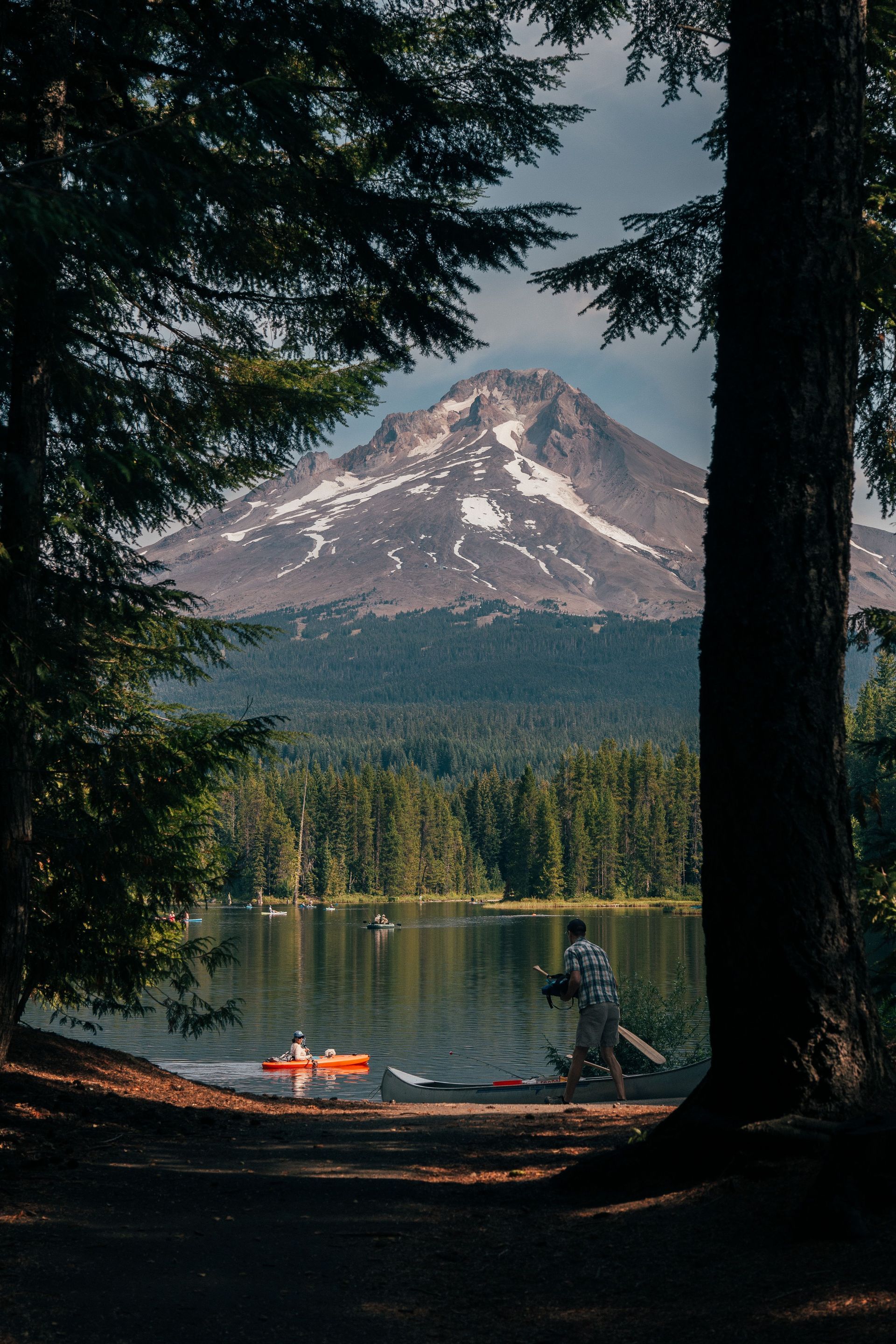Mountain above a forest lake, framed by trees, with two orange kayaks on the water at sunset