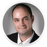 Man in suit smiles at the camera in front of a neutral background.