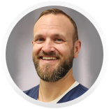 Man with a full beard smiling, wearing a blue shirt.