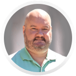 Bald man with beard wearing a light green collared shirt, smiling, in front of a neutral-colored background.